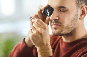 Close up of young man carefully examining diamond ring through magnifying glass. Jewelry expert or...