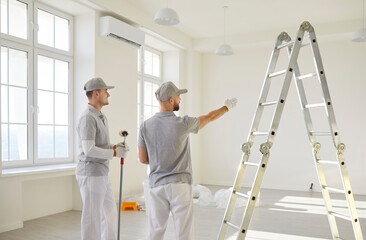 Two male painters planning apartment redecoration, standing backs to camera with painting...