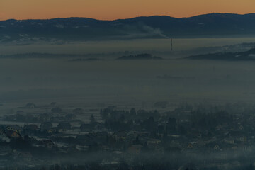 Winter mountain valley with village covered in smog at sunrise