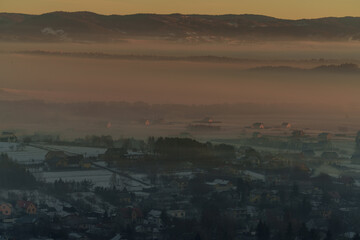 Winter mountain valley with village covered in smog at sunrise