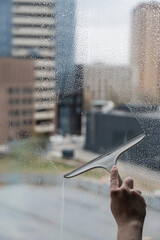 A woman washes a window with a scraper. 