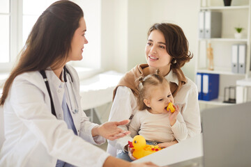 Doctor pediatrician or nurse attending to a mother and young daughter during a medical consultation...