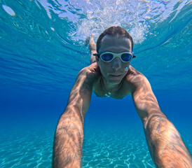 Fototapeta premium Man swimming underwater in the Mediterranean sea off the Sicilian coast. The man is forty years old, of caucasian origin and has swimming goggles on his face
