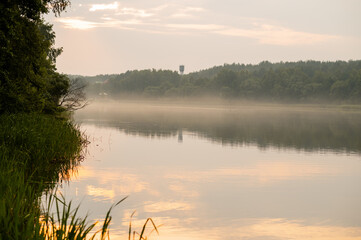 Tranquil misty river landscape at sunrise, with soft golden light reflecting in the calm water and...