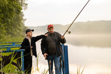 Father teaching his son how to fish on a calm foggy lake, sharing a peaceful and meaningful bonding...