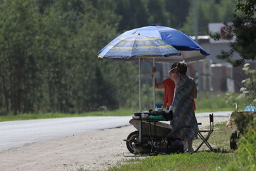 Women at tables under umbrellas prepare goods for roadside trade