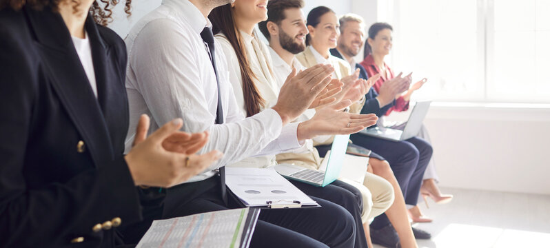Cropped view of professional team sitting in row in conference room, applauding to speaker. Group of business people engaged in business meeting, presentation, celebrating successful event. Banner.