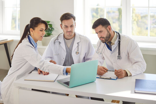 Group of a concentrated doctors and nurses working together in a clinic office during a meeting, using a laptop for team discussions and teamwork to enhance medical care and efficiency.