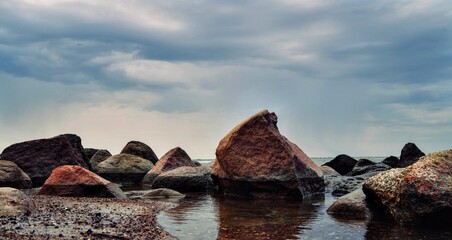 Dramatic coastal landscape with large weathered boulders by the sea under a moody, cloudy sky. The...