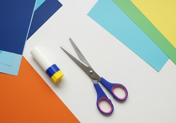 Overhead shot of scissors, glue stick, and colorful construction paper on a white surface.