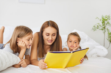 Happy family reading in bed, parents and cute small kids laughing lying together, children bonding with mother having fun enjoy funny moments in bedroom, mum telling small kid funny fairy tale story 