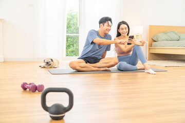 Obraz premium Happy Asian family couple using smartphone tracking health and fitness after sport training workout exercise in living room. Man and woman enjoy healthy wellness lifestyle with healthtech at home.