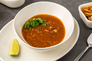 Spicy Mexican chicken soup with noodles, garnished with fresh cilantro and lime wedge