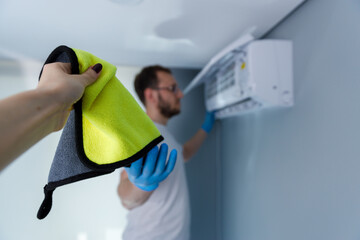A Man Cleaning an Air Conditioner with a Cloth: The Importance of Maintenance for Optimal Air...