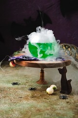 Halloween concept, boiling magical green potion in round glass pot with white smoke on wooden stand