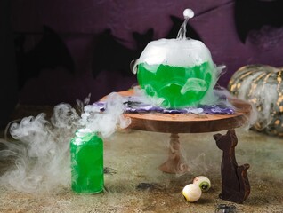 Halloween concept, boiling magical green potion in round glass pot with white smoke on wooden stand