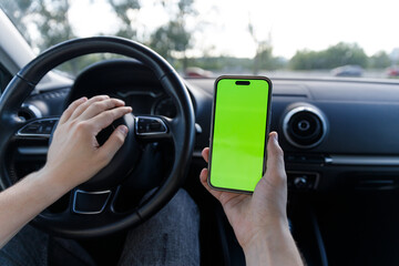 Occupant in Vehicle Holds Smartphone Displaying Green Screen While Steering, Demonstrating Modern...
