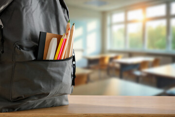 School backpack with supplies on classroom desk – back to school and education concept with...