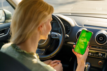 Woman with blonde hair sitting in car, holding a phone with a vibrant green background displaying a...