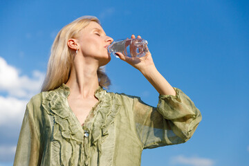 Refreshing Hydration: A Woman Enjoying Water Under a Bright Blue Sky in a Soft Green Blouse with...