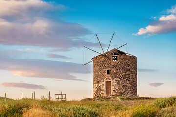 Traditional Greek windmill rising majestically in a field, illuminated by the warm glow of a...