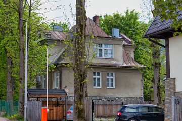 A beige house with a red roof sits peacefully among lush trees. A parked car and nearby fence hint at quiet domestic life in Zakopane - Lesser Poland - Poland