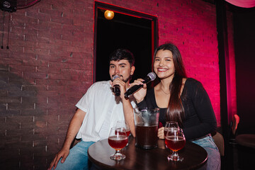 LGBT friends holding a microphone singing in a bar or cafe sitting at a table with beer