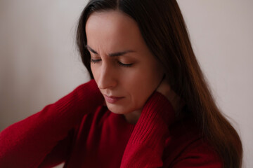 Young woman in red sweater holding her neck with eyes closed, showing discomfort or neck pain,...