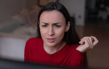 Young woman in red sweater looking at screen with a confused and questioning expression while...