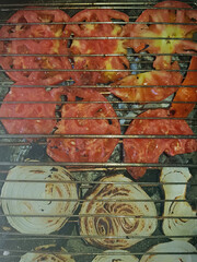 A close-up view reveals onions and tomatoes roasting to perfection on the grill, their flavors melding together in a culinary delight.