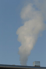 There is smoke billowing out of a brick chimney, contrasting sharply against the clear blue sky above, creating a striking visual scene