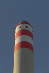 A vivid red and white striped chimney stands tall against the backdrop of a clear blue sky, creating a striking visual contrast