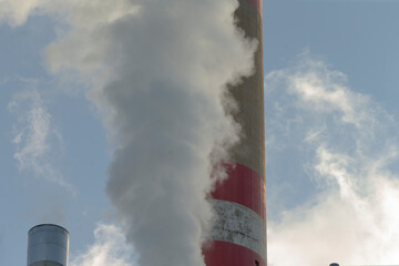 A vibrant red and white chimney is emitting smoke into the atmosphere, signifying industrial activity nearby