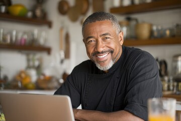 Fototapeta premium Confident Mature African American Man Engaged in Work on Laptop at Kitchen Table