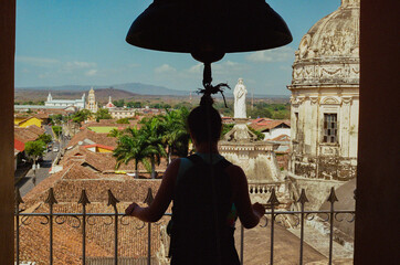 A silhouette of a woman appreciating the scenic colonial architecture from a balcony view,...