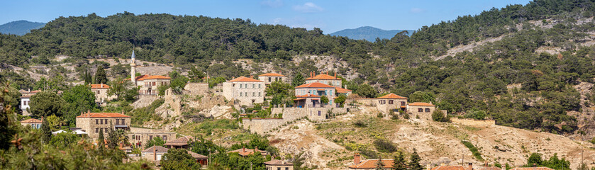 Fototapeta premium Picturesque view of Adatepe village, showcasing traditional stone houses nestled amidst lush greenery and rolling hills, creating a serene scene