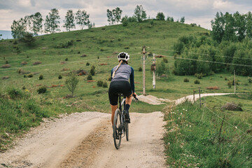 Fototapeta premium Female cyclist rides gravel road through stunning mountain landscape. Epic adventure, scenic views, active lifestyle. Perfect for travel, sports, and nature themes.