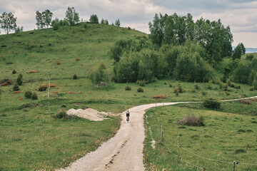 Cyclist on a gravel road winding through a picturesque green landscape. Serene countryside scene...