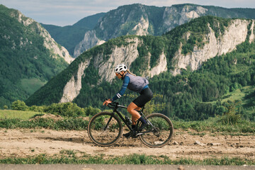 Female cyclist rides gravel bike through scenic mountain pass.  Epic landscape backdrop. Active lifestyle, adventure, freedom.