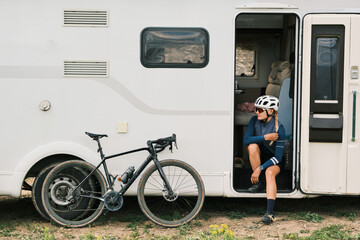 Female cyclist takes a break, resting by her bike and campervan.  Perfect for travel, adventure, and active lifestyle themes.