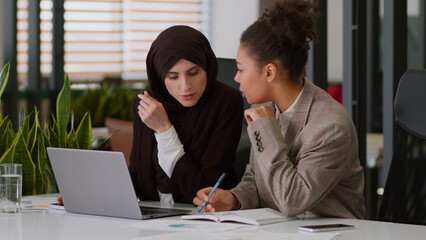 Multiracial teamwork happy women girls female coworkers office colleagues multiethnic business partners African Muslim businesswomen corporate coaching write notes work laptop consult discuss startup