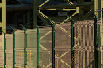 A sturdy fence is surrounding a building that has a train moving in the background, adding an...