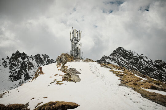 Cell tower atop a snow-covered mountain peak. Dramatic clouds and rugged terrain create a stunning winter landscape. Perfect for technology, nature, and environmental themes.