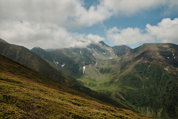 Majestic mountain range shrouded in clouds. Lush green slopes meet the sky in a breathtaking...