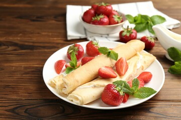 Tasty crepes with cream, strawberries and mint on wooden table, closeup