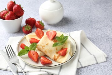 Tasty crepes with cream, strawberries and mint served on light gray textured table, closeup