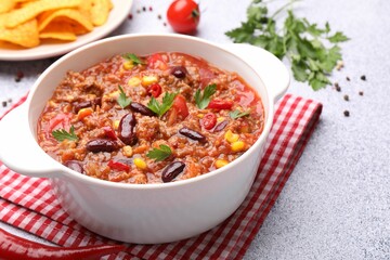 Tasty chili con carne in bowl, nachos and ingredients on grey table, closeup