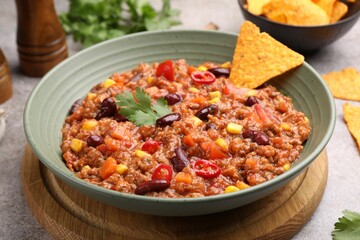 Tasty chili con carne in bowl and nachos on grey table, closeup
