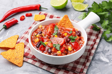 Tasty chili con carne in bowl and nachos on grey textured table, closeup