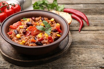 Tasty chili con carne in bowl and ingredients on wooden table, closeup. Space for text